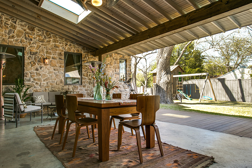 Outdoor dining table in a Texas farmhouse’s backyard, featuring beautiful stone walls and a wooden roof.